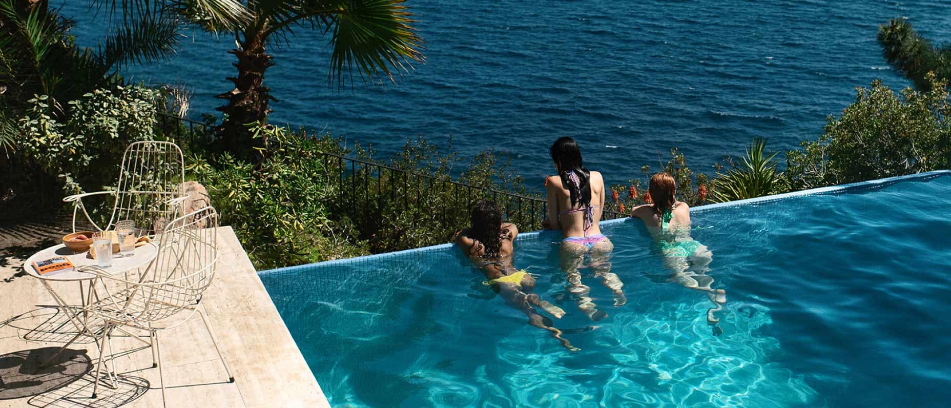 Des amis se reposent et profitent de la vue au bord d’une piscine à débordement surplombant l’océan.