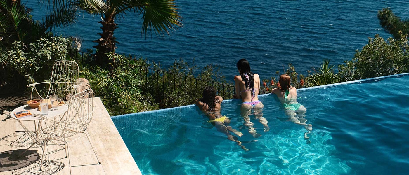 Des amis se reposent et profitent de la vue au bord d’une piscine à débordement surplombant l’océan.