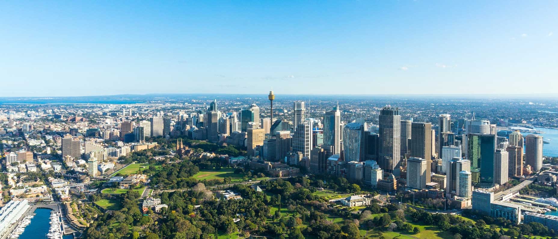 Aerial view of Sydney’s skyline with high-rise buildings, green parkland and surrounding harbour.