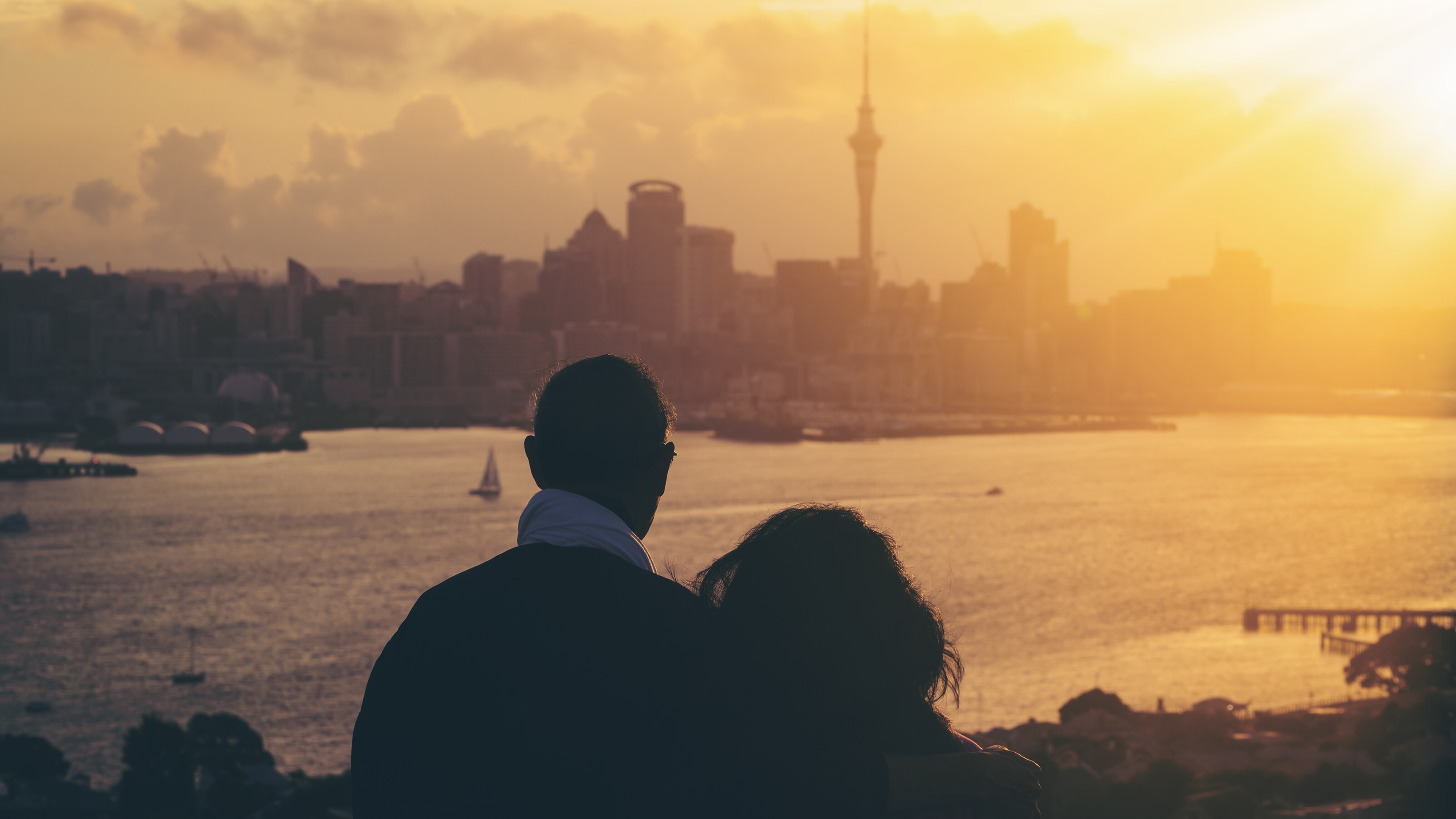 Happy senior couple watching sunset in Auckland city skyline with city center and Auckland Sky Tower in New Zealand.