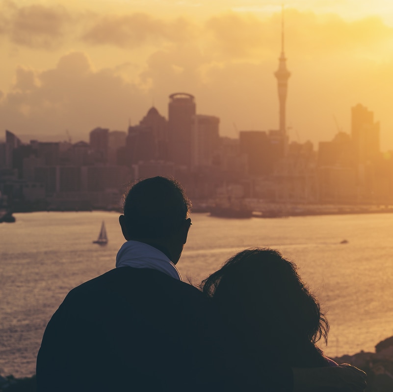 Happy senior couple watching sunset in Auckland city skyline with city center and Auckland Sky Tower in New Zealand.