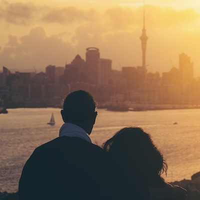 Happy senior couple watching sunset in Auckland city skyline with city center and Auckland Sky Tower in New Zealand.