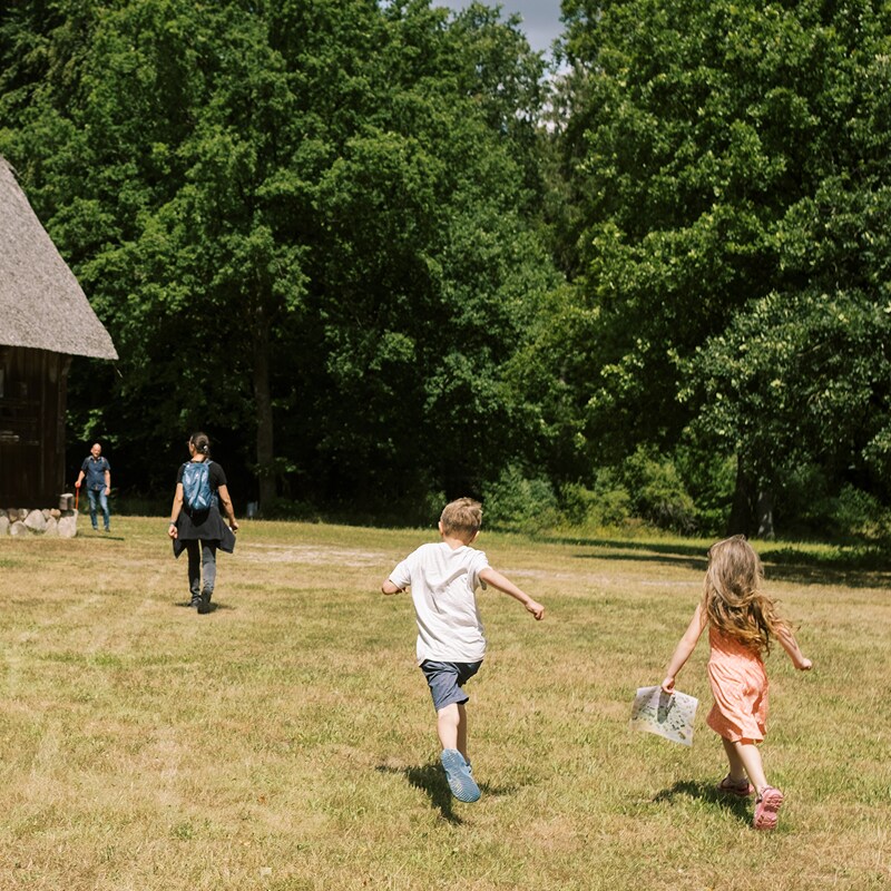 Zwei Erwachsene und zwei Kinder gehen über den Rasen rund um ein Haus, vor dem Hintergrund üppiger Bäume.