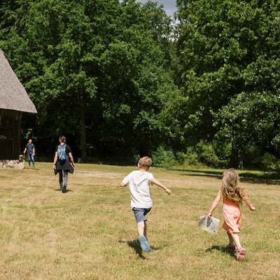Zwei Erwachsene und zwei Kinder gehen über den Rasen rund um ein Haus, vor dem Hintergrund üppiger Bäume.