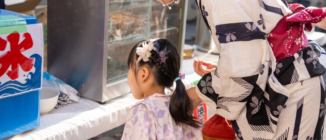 An adult and child in traditional Japanese dress at a food stall in Tokyo.