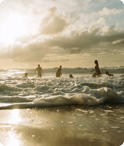 Un groupe de personnes s’amuse dans l’océan. Le soleil brille en arrière-plan. 