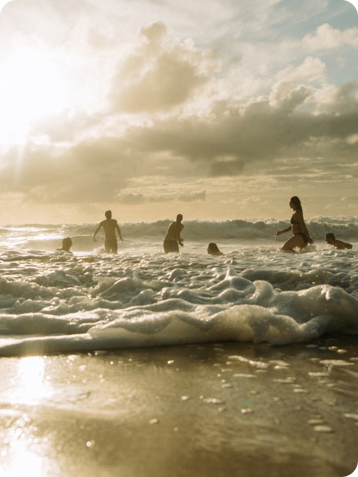 A group of people playing in the ocean. The sun is shining in the background. 