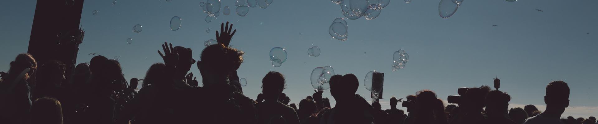 Une foule de gens lève les mains vers le ciel bleu, avec des bulles flottant dans l’air.