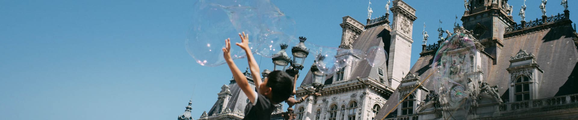 A crowd of people with their hands up and blue skies above them. Bubbles are floating in the sky.