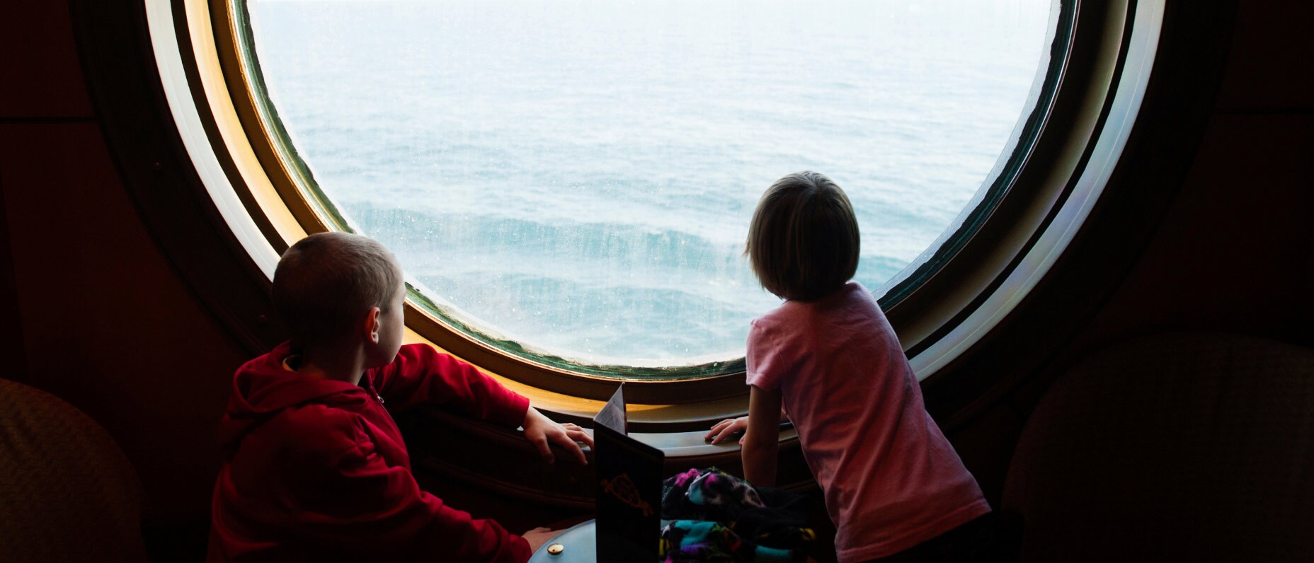 Two children looking out at the ocean through an oversized porthole.