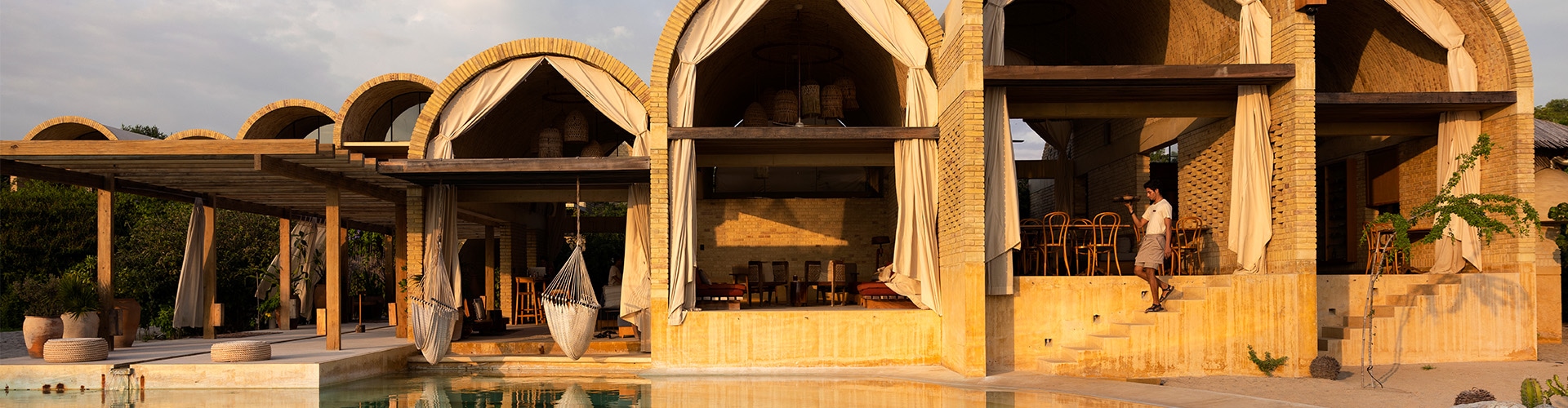A beautiful modern hotel with arches looks out over a pool with someone walking down some sunny steps.