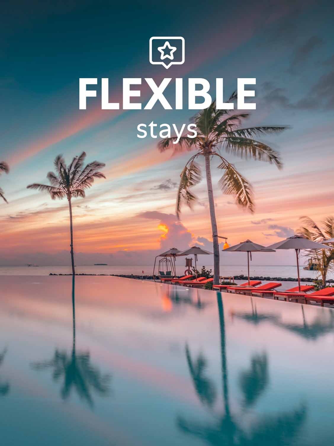 A perfectly still ocean-side swimming pool is reflecting the palm trees above and empty poolside umbrellas at night. A superimposed title reads: Flexible stays