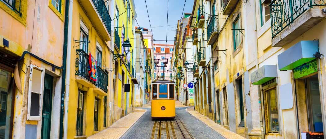 Ground view of a colorful street on a hill in Lisbon, Portugal, with a street car heading down the hill and facing the camera.