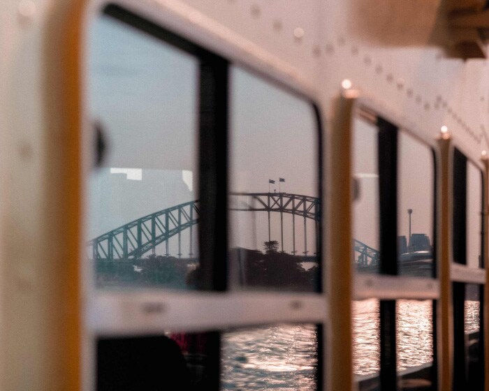 Sydney Harbour Bridge is reflected in the windows of a ferry as the sun sets.