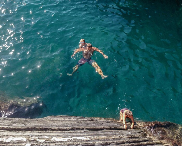 A person wearing goggles swims in the ocean and two children play and swim around them.