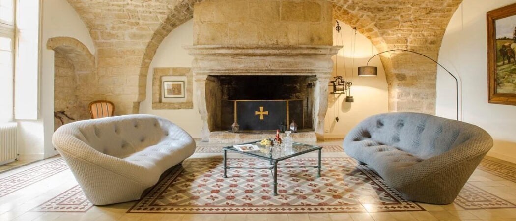 Interior view of two luxurious couches in front of a large stone fireplace at the Château De Valjoyeuse in Montagnac.