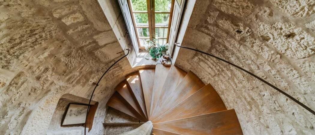 Top-down view of a spiral staircase at the Château D'Ax in Porte-du-Quercy. A single window looks out to a garden.