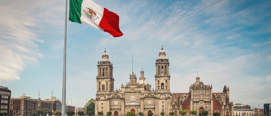 The sun rises over the Mexico City Metropolitan Cathedral in Zocalo Square. The national flag flies in the foreground.