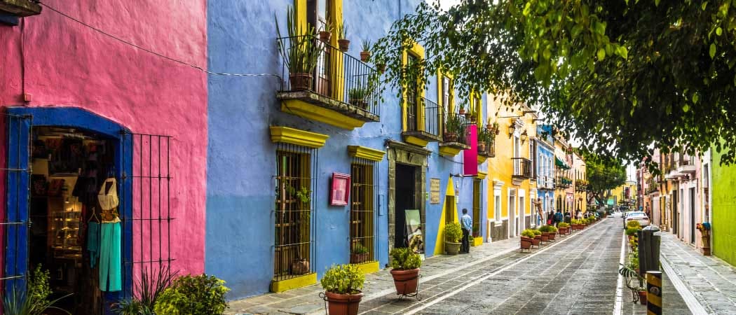 An exterior view of a narrow street lined with buildings painted in bright colors and plants in terracotta pots.