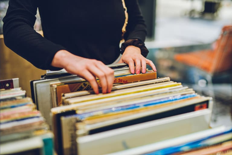 A person in a black top stands in front of a collection of vintage records and flips through them one by one.