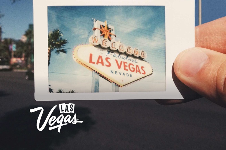 A close-up view of someone holding a small Polaroid photograph of the neon sign that reads