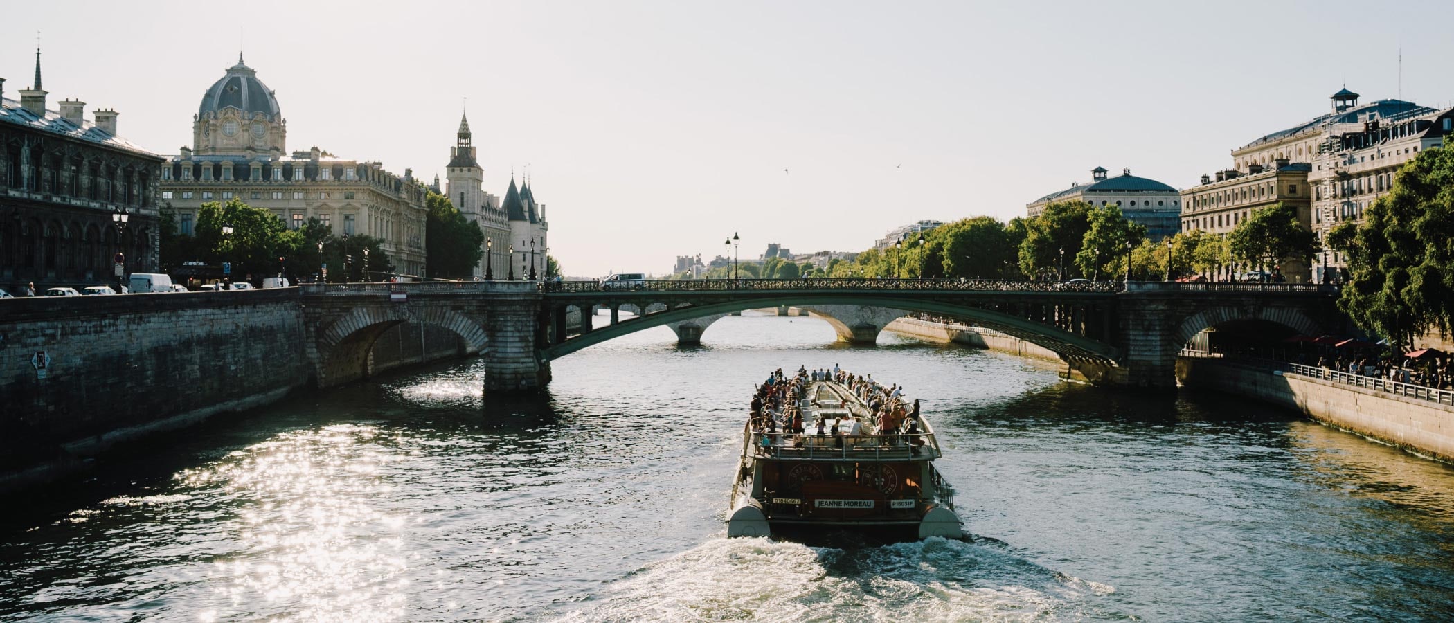 A boat filled with people sails on the sparkling waters of the River Seine in Paris.