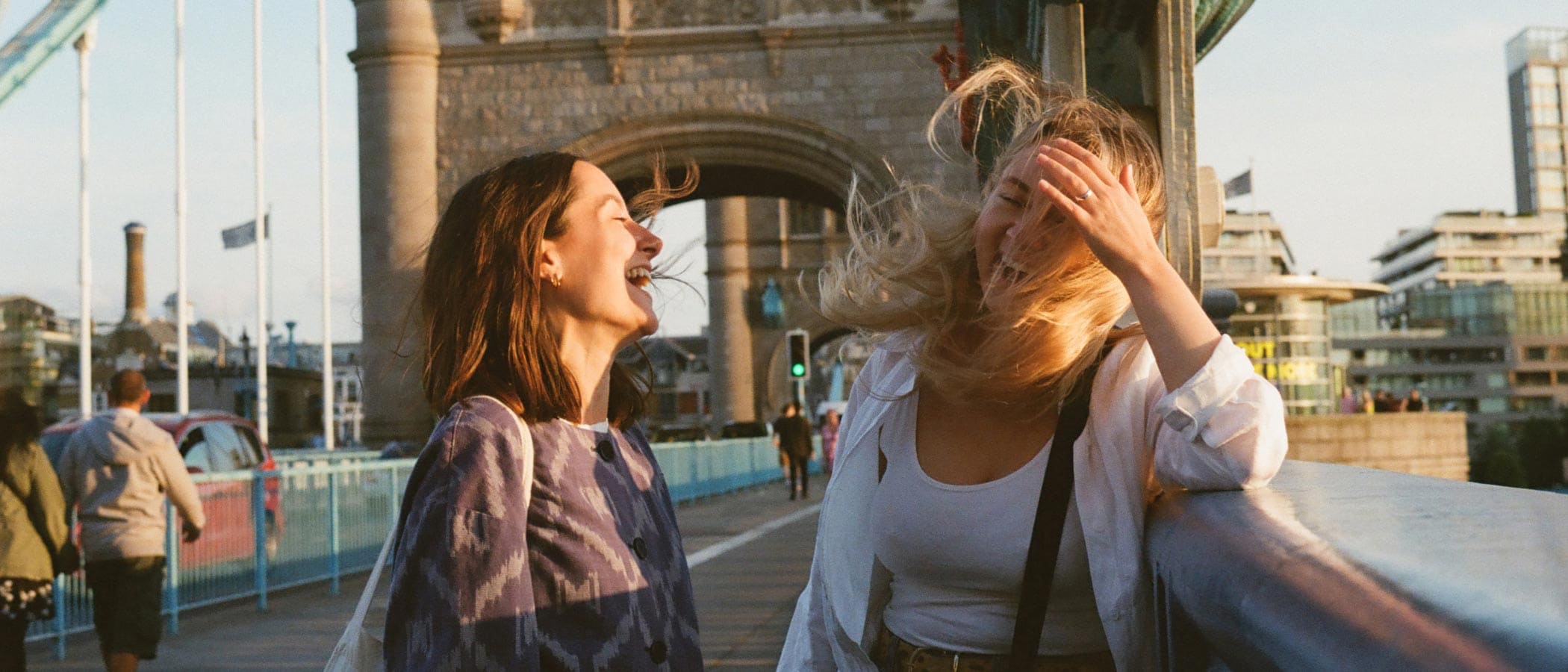 Two people stand on Tower Bridge and laugh as the wind blows their hair.