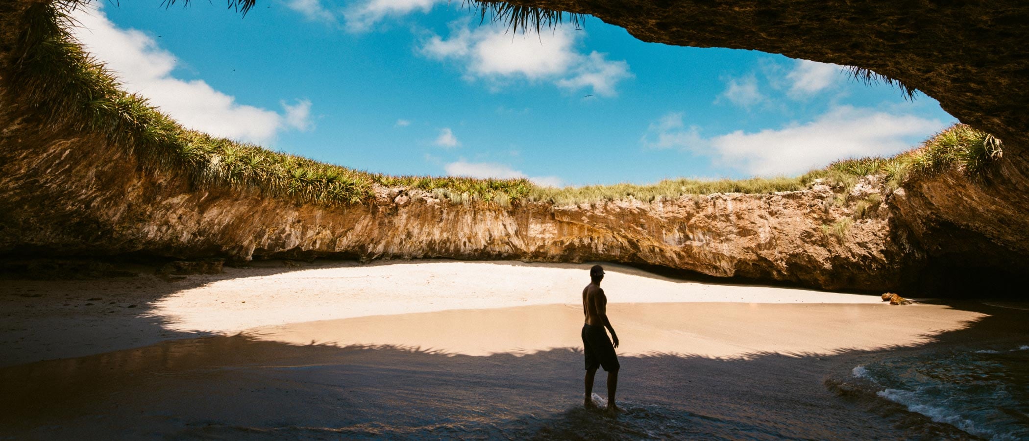 Shaded by a cove, a person walks on a beach on a sunny day in Puerto Vallarta.