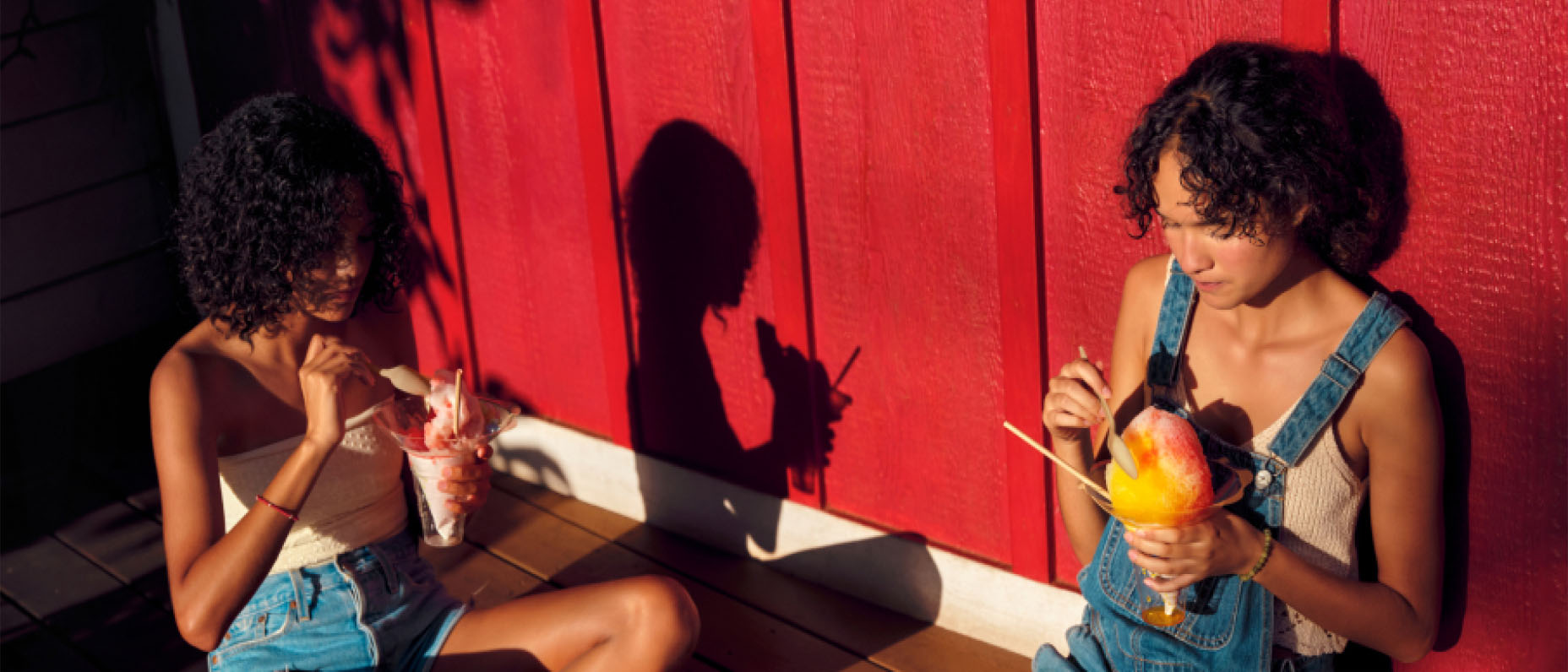 People sitting outdoors on a large wooden deck eating frozen treats in the sunshine.