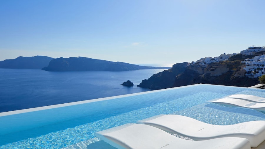 White lounge chairs sit in a blue infinity pool overlooking the Aegean Sea at the Canaves Oia Suites in Santorini Greece.