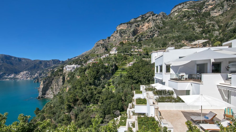 The white angular buildings of Casa Angelina in Praiano Italy rest against tree-covered cliffs by the Amalfi Coast.
