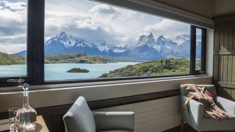 At Explora Patagonia in Chile a wide window in a hotel room reveals Torres del Paine National Park’s mountains and a lake.