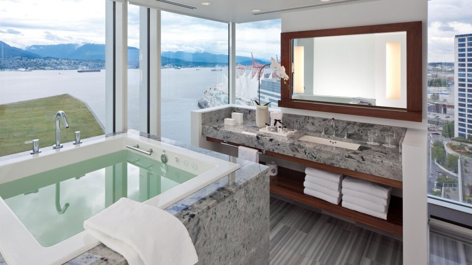 A spacious hotel bathroom with a private marble hot tub overlooks the harbor at the Fairmont Pacific Rim in Vancouver.