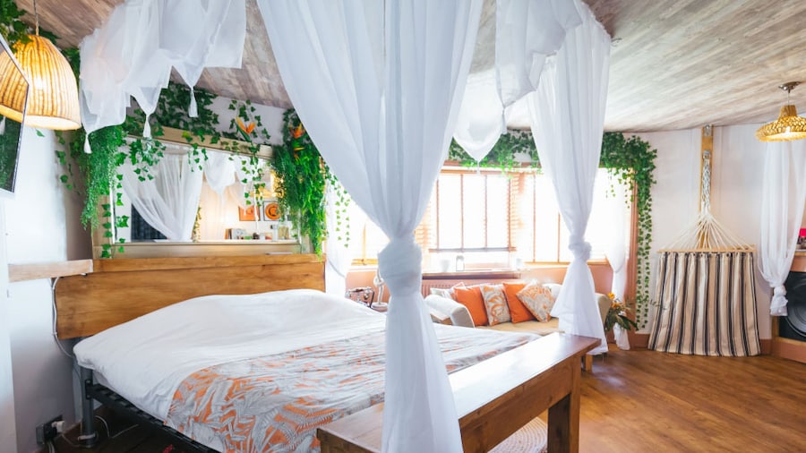 A room at Hotel Pelirocco in Brighton England has a bed with a white canopy fake ivy on the walls and a hammock.