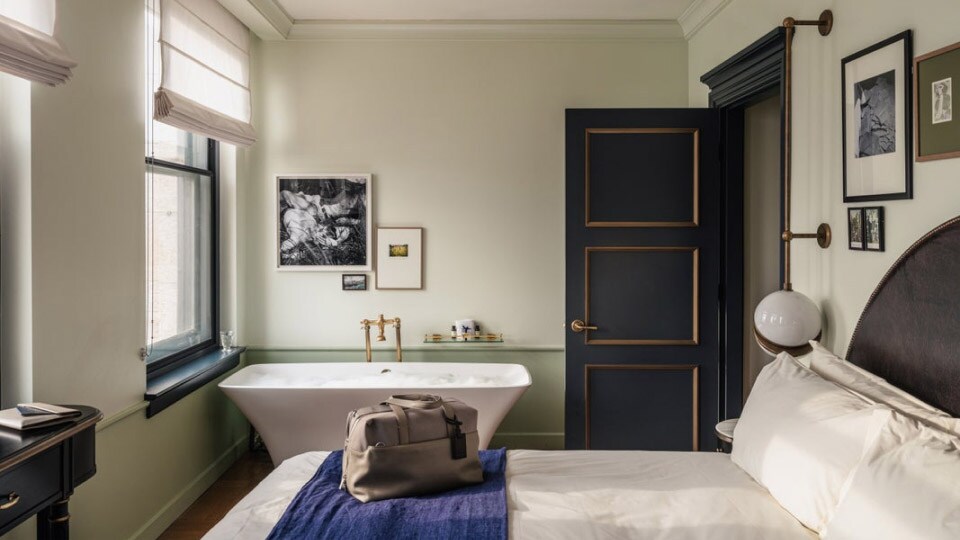 At the Hotel Per La in Los Angeles a door opens to a small room with a bathtub by an open window a bed and a desk.