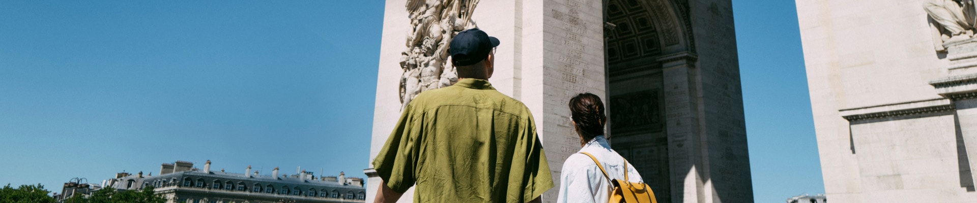 Dos personas en un viaje internacional están viendo el Arco del Triunfo de París durante un día soleado.