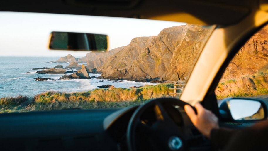The view through a car windscreen, looking out over a rocky bay.
