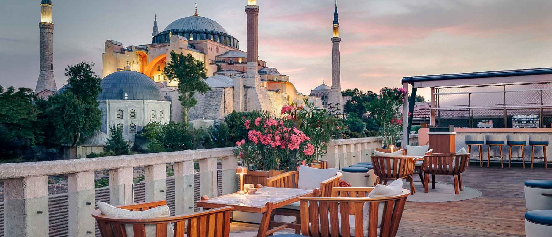 İstanbul'da, dinlenme salonunda ahşap mobilyaların bulunduğu bir otel terasından Sultanahmet Camii gün batımı manzarası.