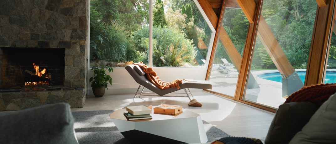 A modern lounge chair sits in front of a large glass window, overlooking a  garden with a pool.