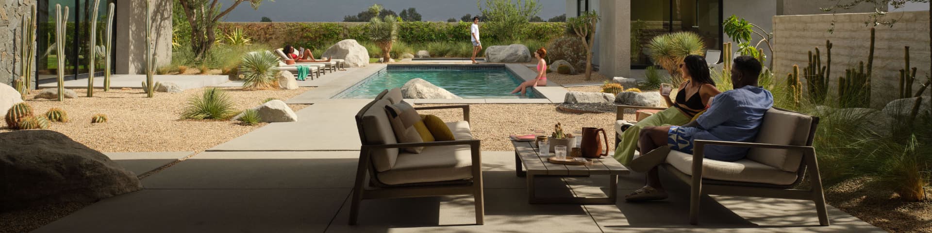 Five travelers enjoy a huge backyard with a beautiful pool, spacious seating area, and serene desert landscaping.