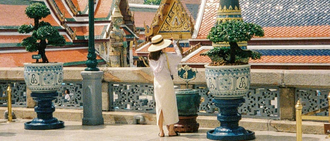 Une personne portant une robe blanche et un chapeau regarde le Grand Palais doré de Bangkok 
