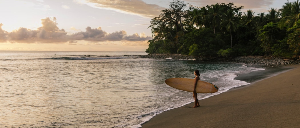 Une personne regarde l’océan depuis une plage du Costa Rica et tient une planche de surf