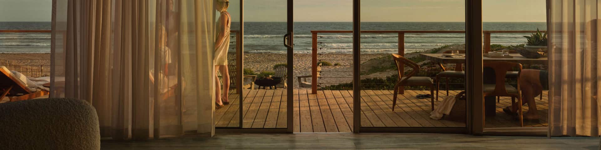 Ein Ausblick aus einem Ferienhaus, der vier Urlauber auf einer Terrasse am Strand zeigt.