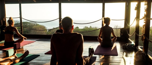 Des personnes assises les jambes croisées dans un studio de yoga en plein air donnant sur l’océan