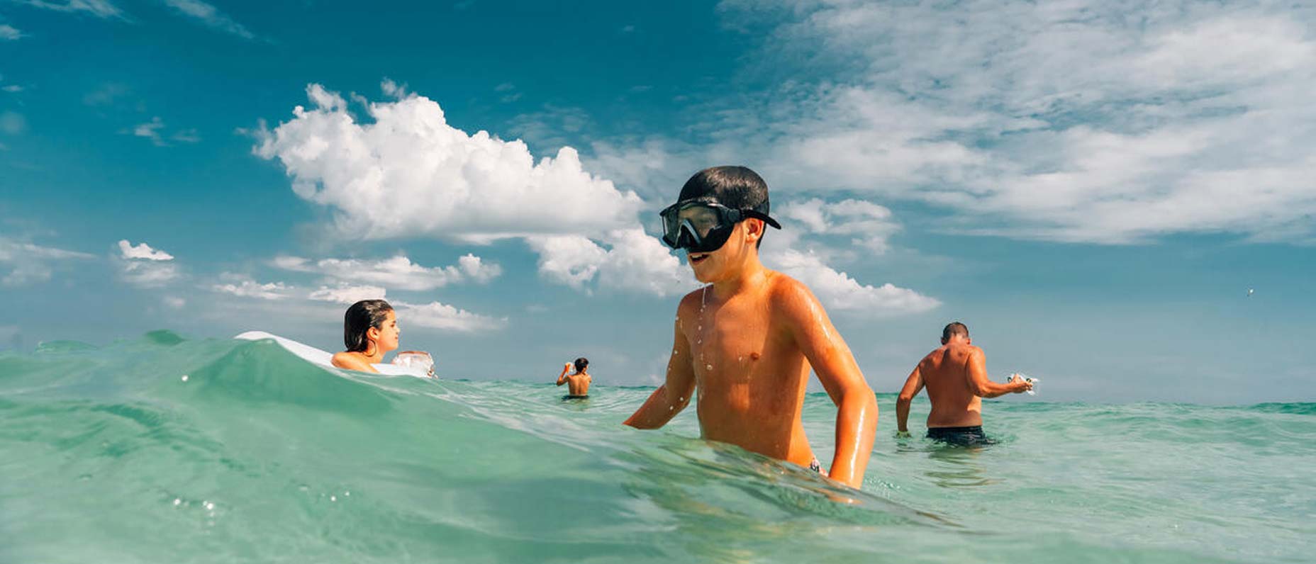 Kids playing in the ocean with sunlight and water droplets creating a summery atmosphere, with text above reading: “Members save 25% or more.