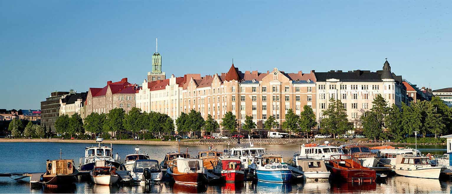 Colorful boats docked in a peaceful harbor with a row of pastel-hued historic buildings behind them in Helsinki, Finland.