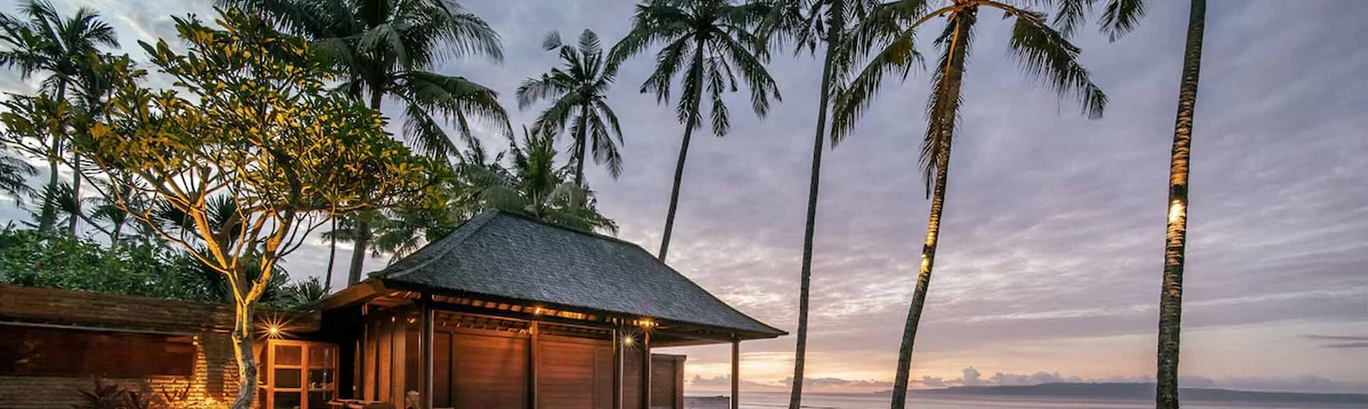 Empty sunloungers line the edge of an infinity pool, looking past palm trees to a calm, tropical ocean.