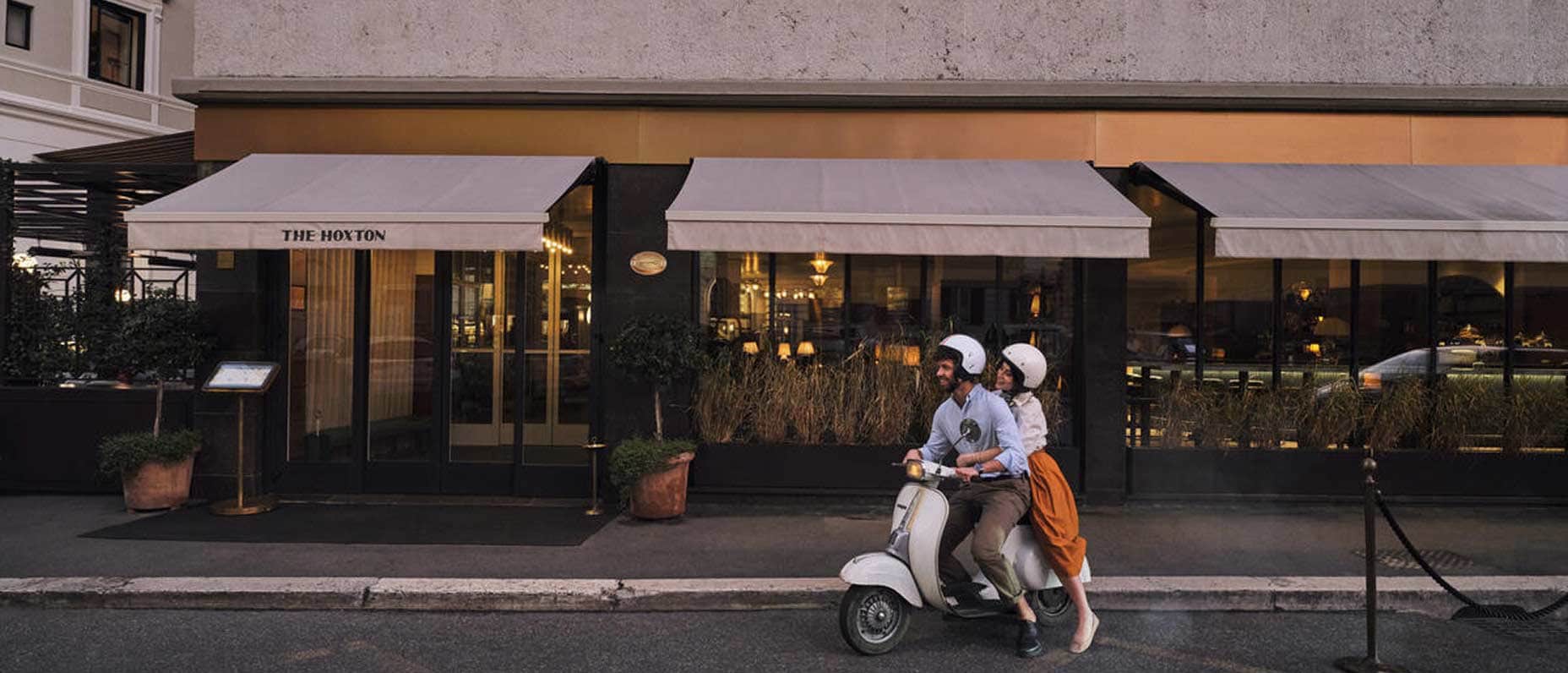 Un couple sur un deux-roues s’éloigne de la devanture d’un restaurant.
