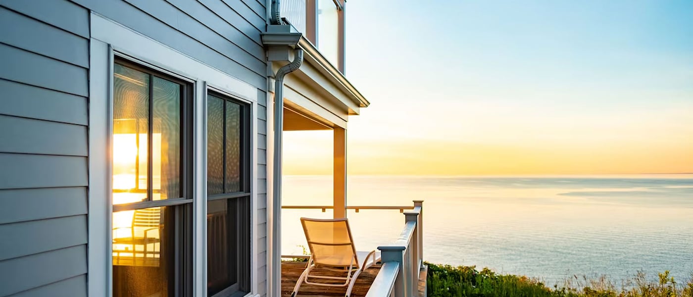 An ocean view from the private veranda of a timber-clad house, where an empty lounger looks out over the sunset.