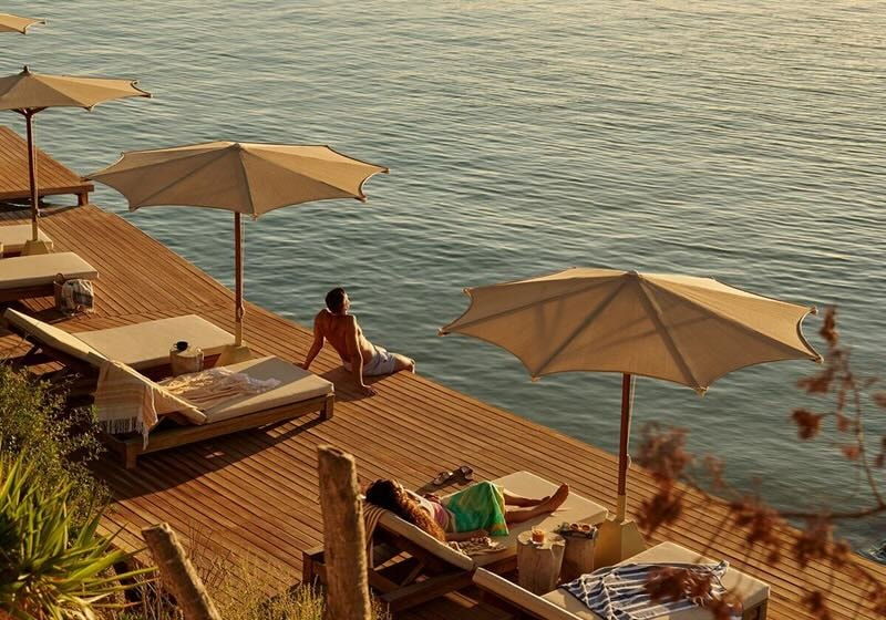 A traveler relaxes on a timber decking that sits over the water at golden hour.